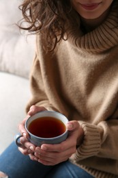 Woman with cup of hot tea indoors, closeup. Cozy home atmosphere