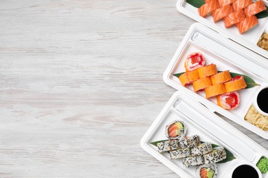 Photo of Food delivery. Plastic containers with delicious sushi on light wooden table, flat lay and space for text