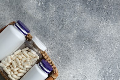 Medical bottles with pills in wicker tray on light gray textured table, top view. Space for text