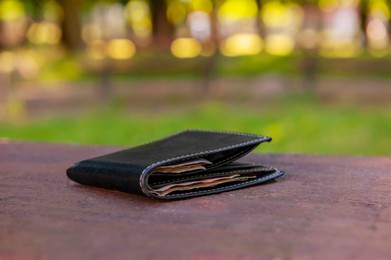 Photo of Black wallet on wooden bench outdoors. Lost and found