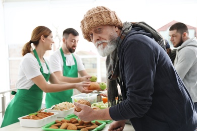 Photo of Senior man with other poor people receiving food from volunteers indoors