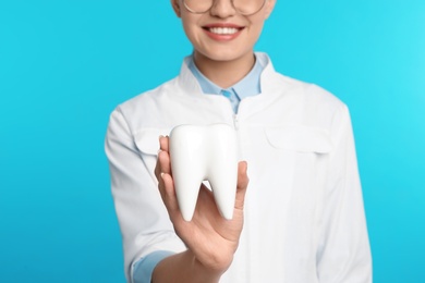 Female dentist holding tooth model on color background, closeup