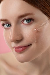Photo of Beautiful woman with freckles applying cosmetic serum onto her face, closeup