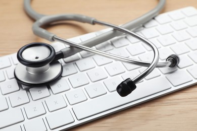 Photo of Computer keyboard with stethoscope on wooden table, closeup
