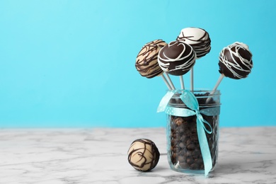 Photo of Yummy cake pops coated with chocolate in glass jar full of coffee beans on table. Space for text