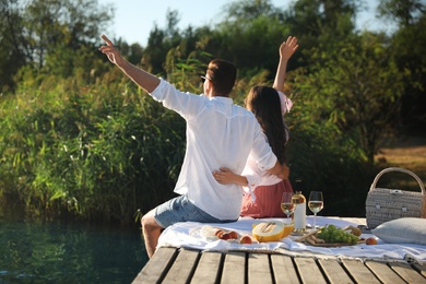 Photo of Happy couple spending time on pier at picnic, back view