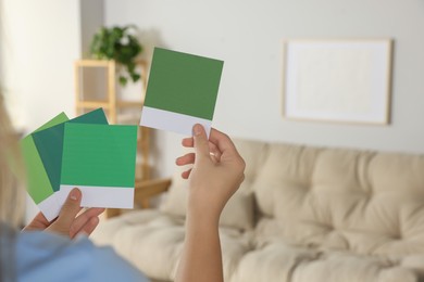 Photo of Woman with color sample cards choosing paint shade for wall in room, closeup. Interior design
