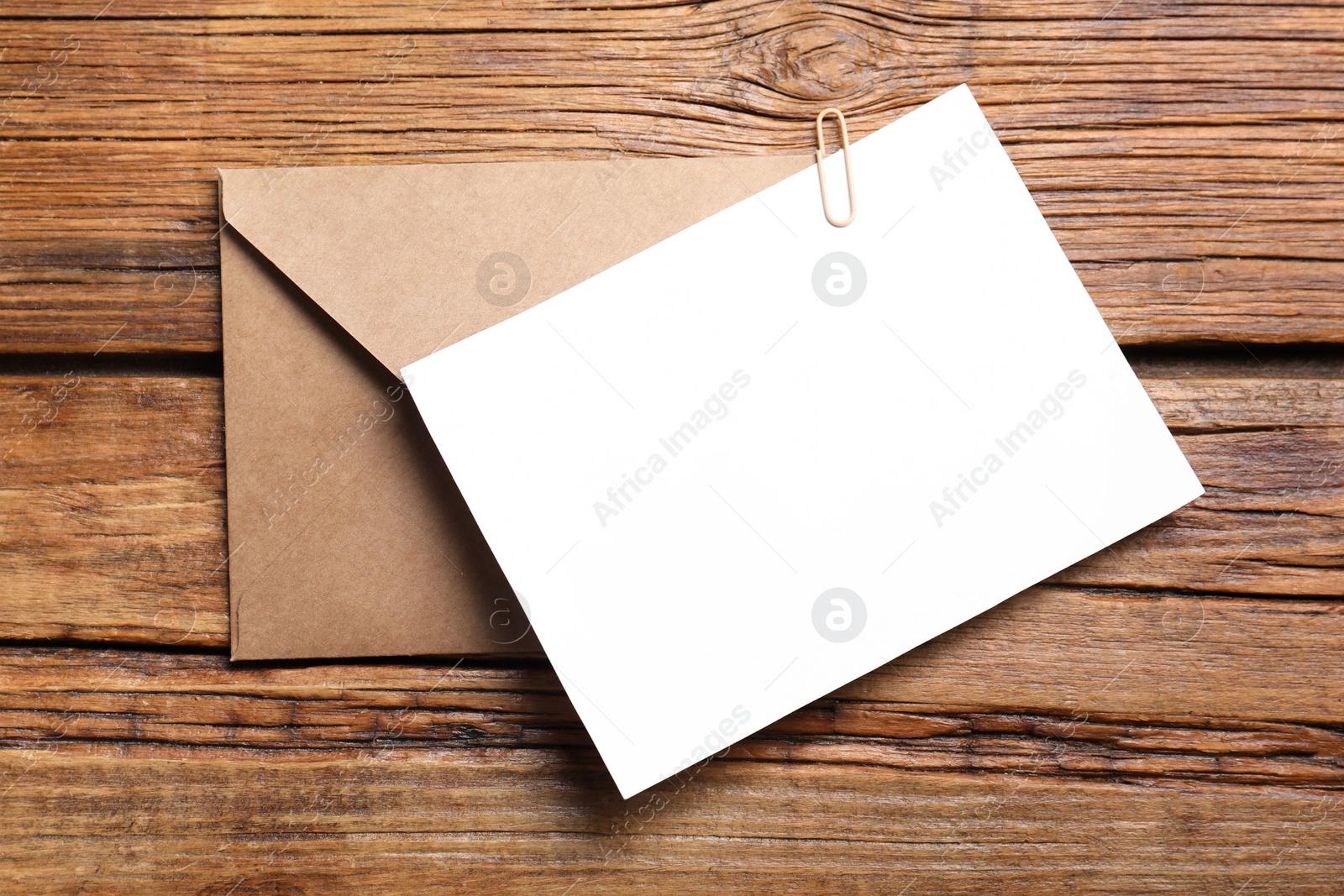 Photo of Blank sheet of paper, paperclip and letter envelope on wooden table, top view. Space for text