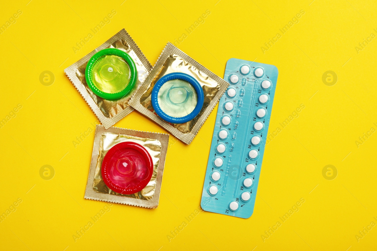 Photo of Condoms and birth control pills on yellow background, flat lay. Safe sex concept