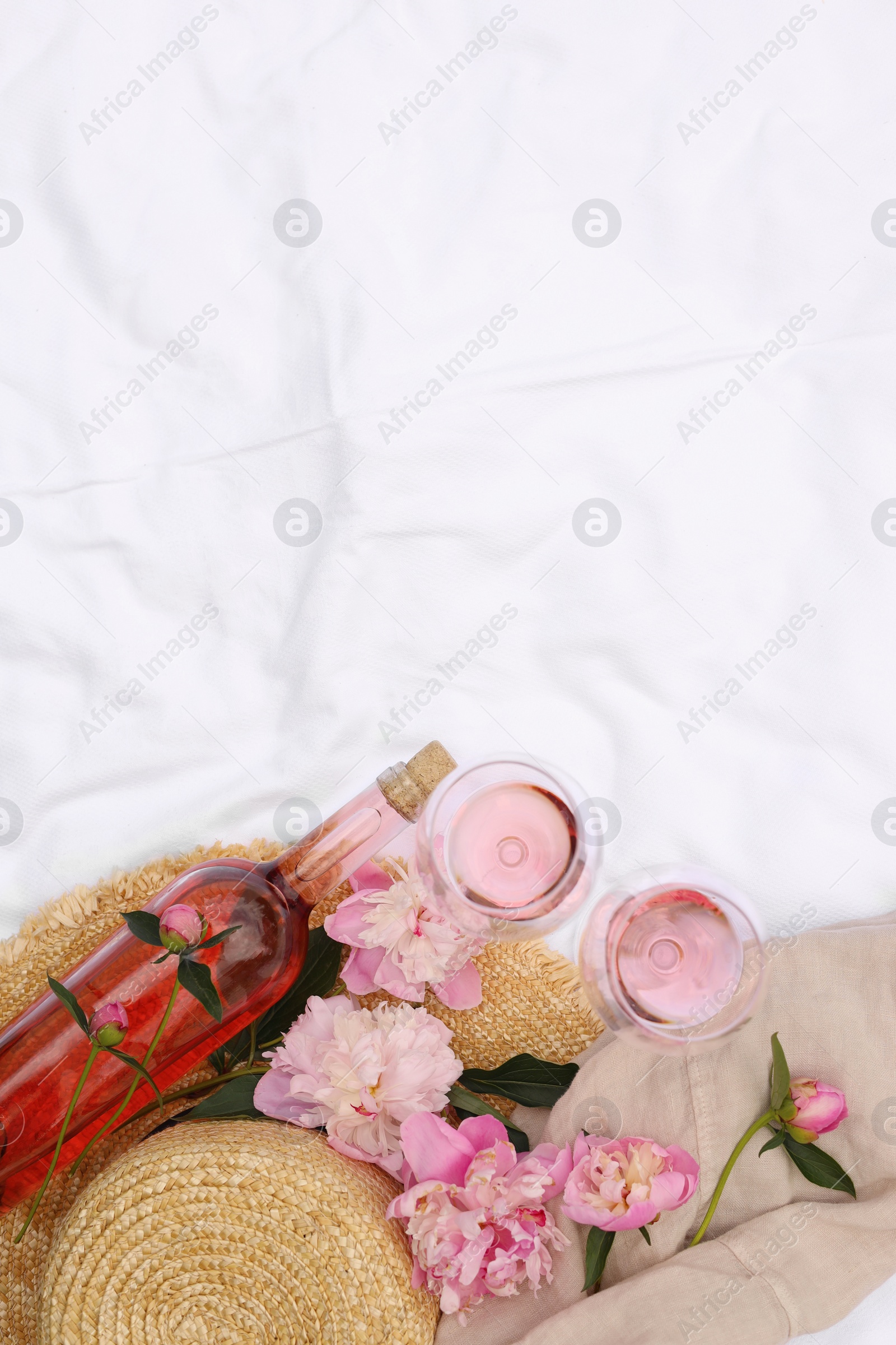 Photo of Flat lay composition with beautiful peonies and rose wine on white fabric, space for text