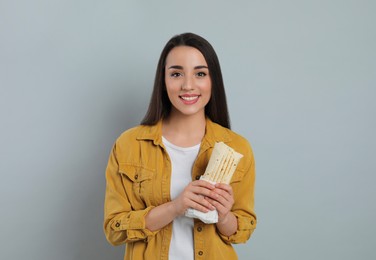 Happy young woman holding tasty shawarma on grey background