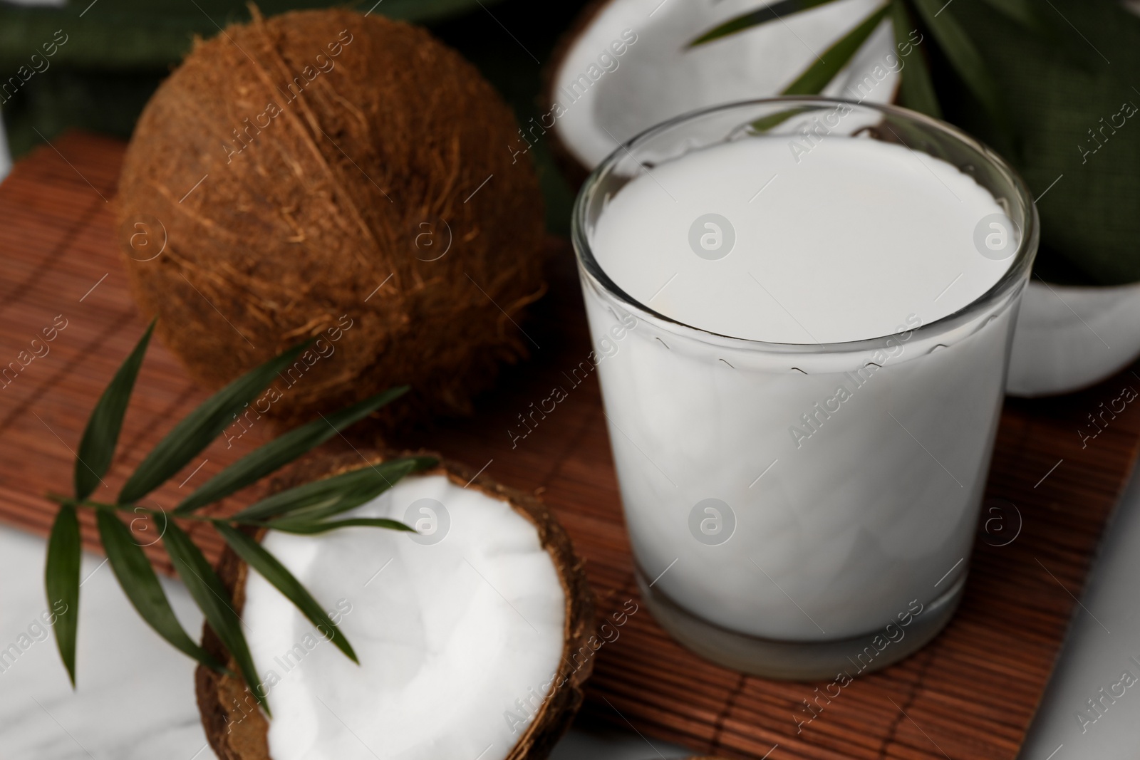 Photo of Glass of delicious vegan milk, coconut pieces and palm leaves on white marble table