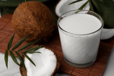 Glass of delicious vegan milk, coconut pieces and palm leaves on white marble table