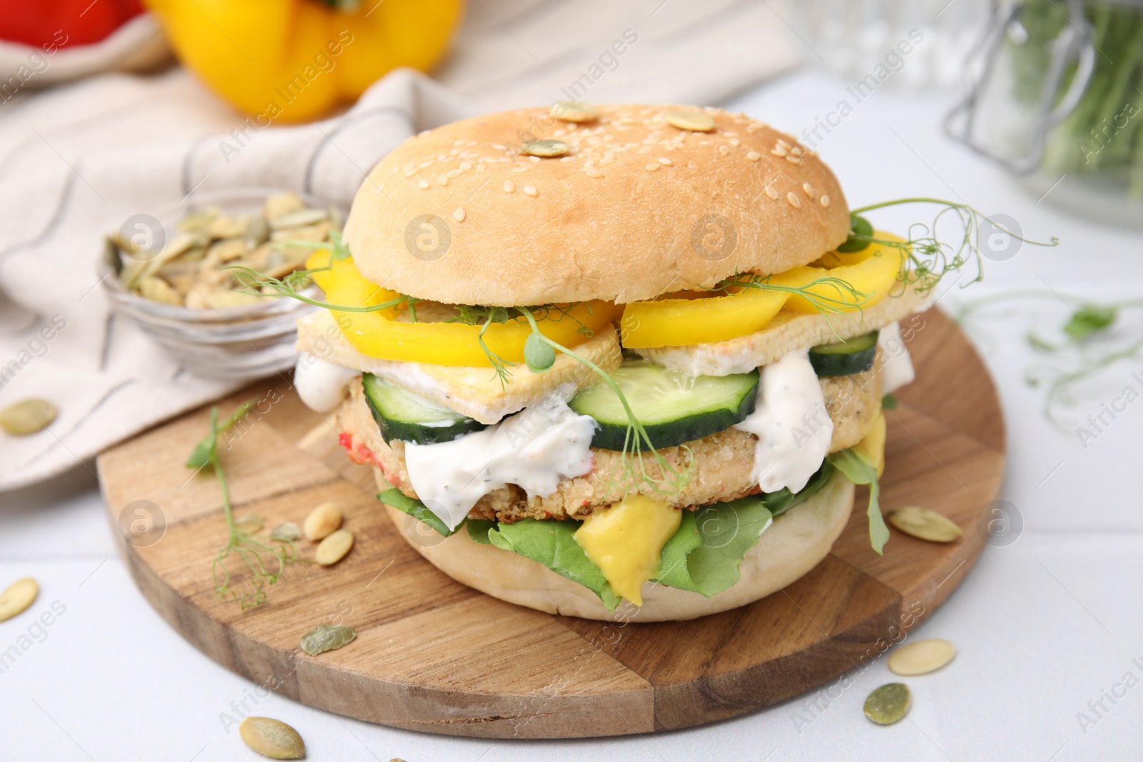 Photo of Tasty vegan burger with vegetables, sauce and patty on white table, closeup