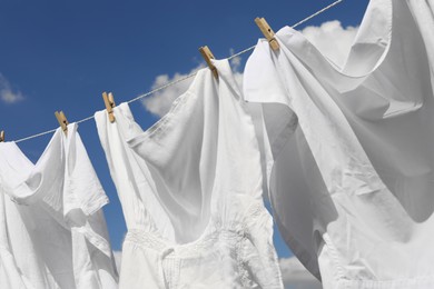 Photo of Clean clothes hanging on washing line against sky, closeup. Drying laundry