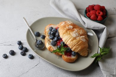 Photo of Delicious croissant with berries, almond flakes and spoon on light grey table