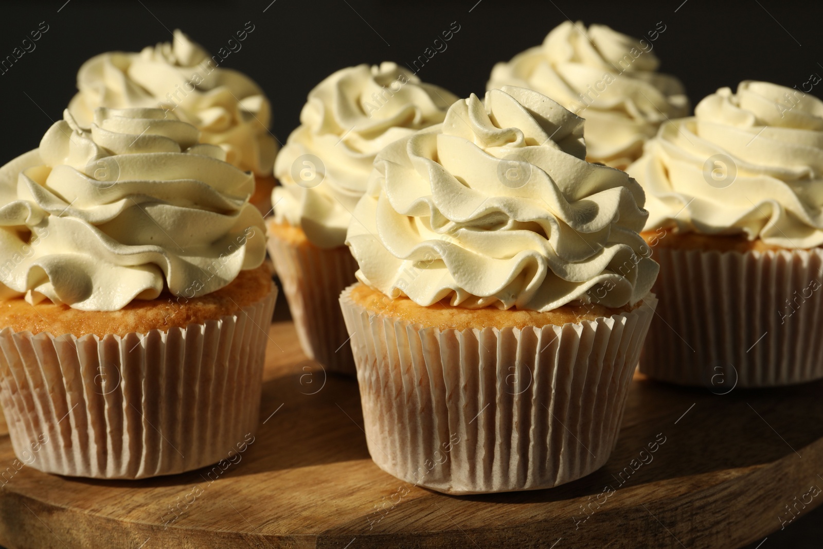 Photo of Tasty cupcakes with vanilla cream on wooden stand, closeup