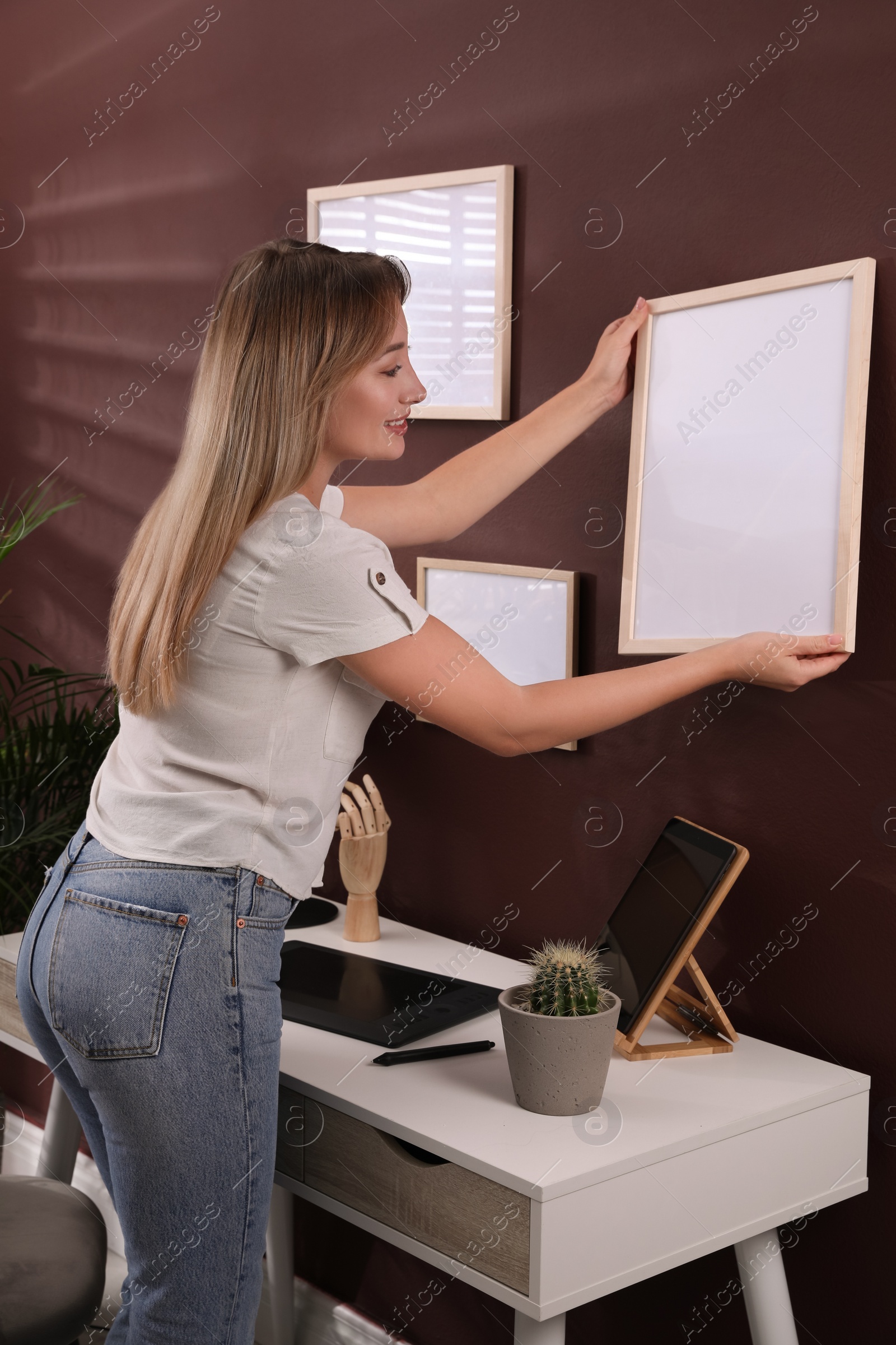 Photo of Young woman hanging empty frame on brown wall indoors. Mockup for design