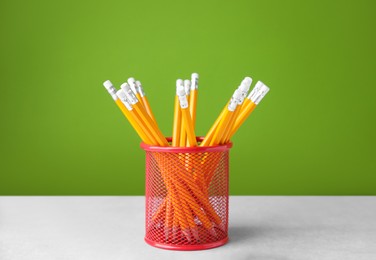 Many sharp pencils in holder on light table against green background