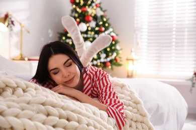 Young woman lying on bed in room with Christmas tree, space for text