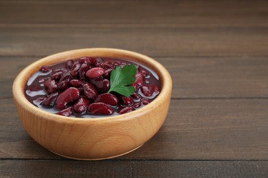 Photo of Bowl of canned red kidney beans with parsley on wooden table, closeup. Space for text
