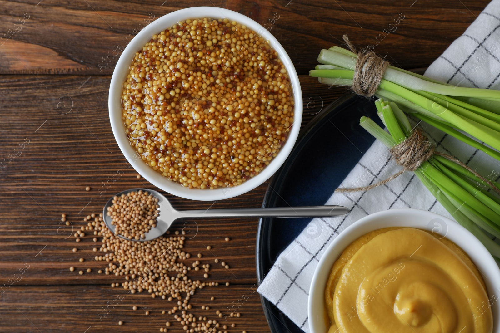 Photo of Delicious whole grain mustard, seeds and fresh green onion on wooden table, flat lay