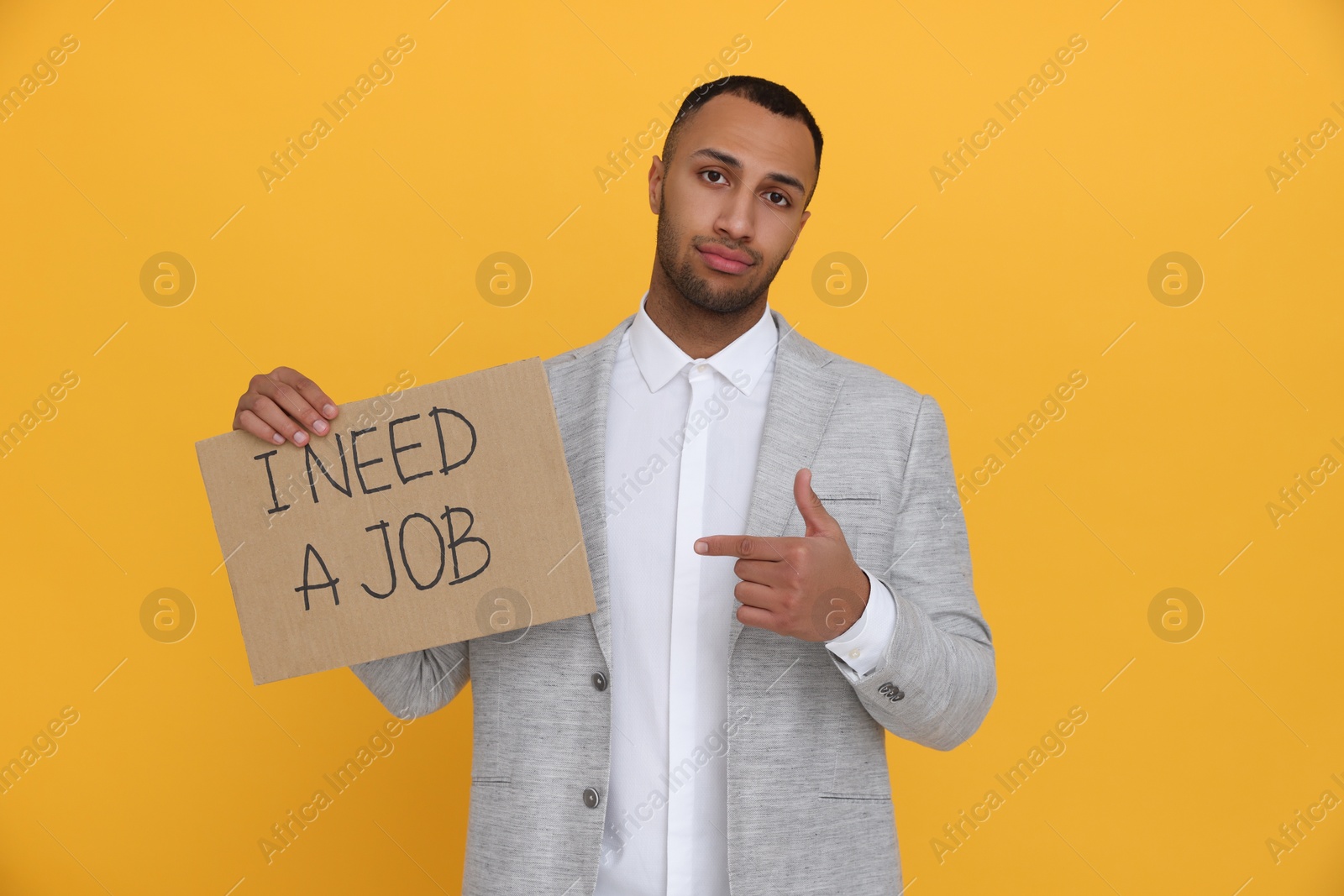 Photo of Young unemployed man holding sign with phrase I Need A job on yellow background