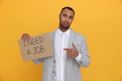 Young unemployed man holding sign with phrase I Need A job on yellow background
