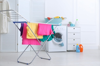 Photo of Clean bright laundry hanging on drying rack indoors