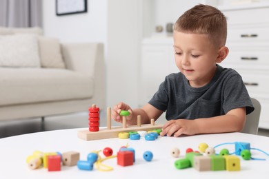 Photo of Motor skills development. Little boy playing with stacking and counting game at table indoors