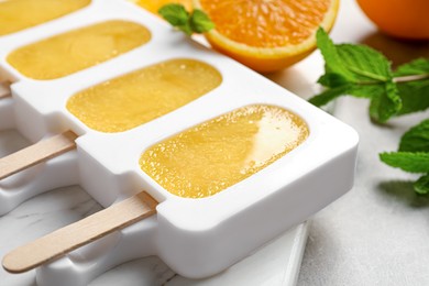 Photo of Tasty orange ice pops in mold on light grey table, closeup. Fruit popsicle