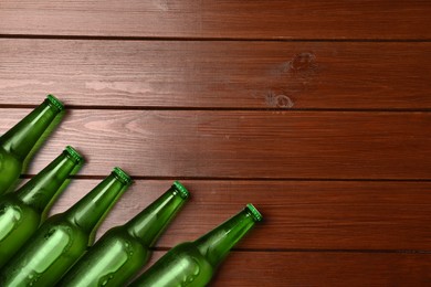 Glass bottles of beer on wooden background, flat lay. Space for text