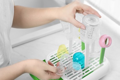 Woman putting baby bottles on dryer after sterilization in kitchen, closeup