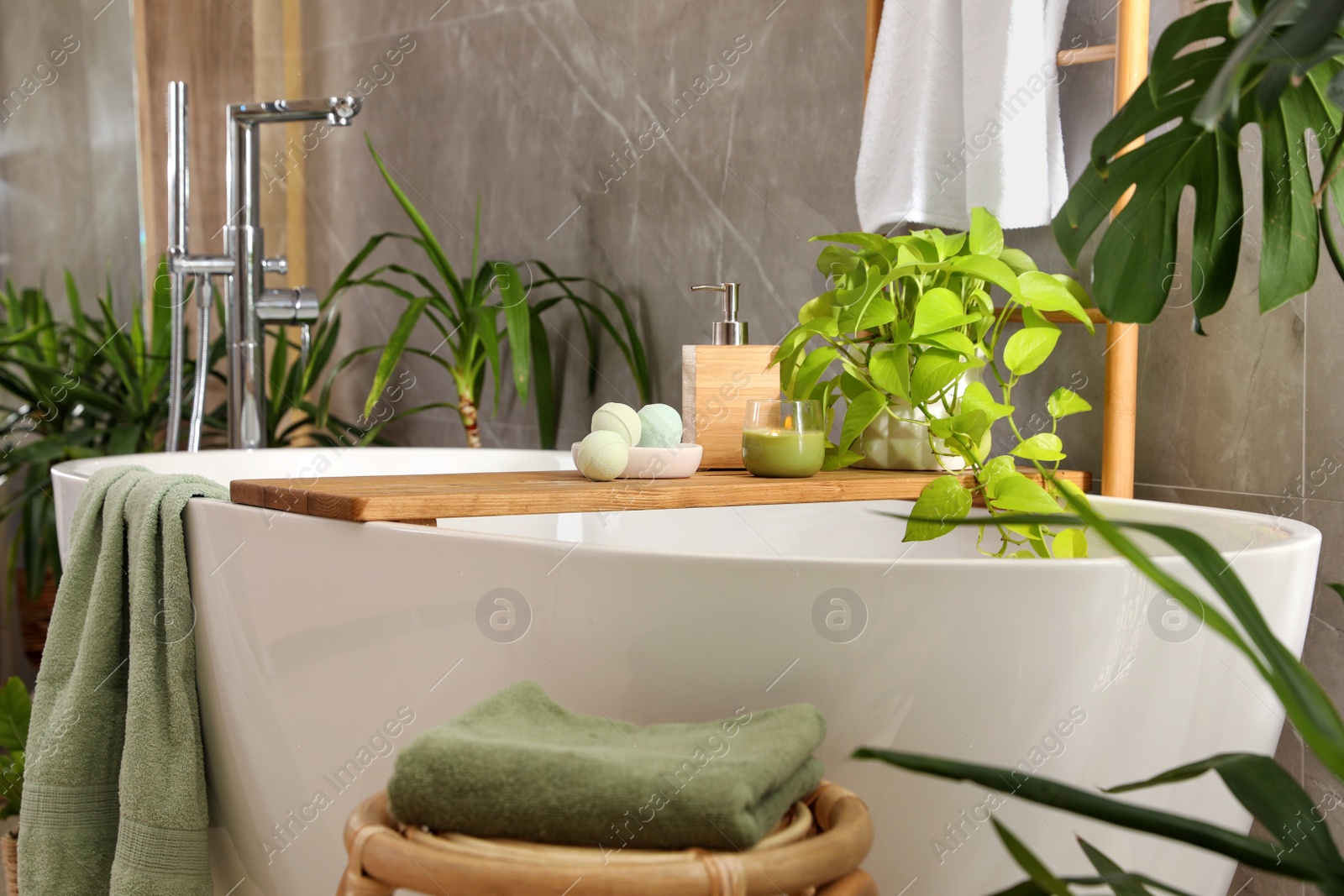 Photo of Modern white tub and beautiful green houseplants in bathroom. Interior design