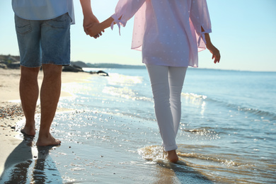 Photo of Young couple walking on beach near sea, closeup. Honeymoon trip