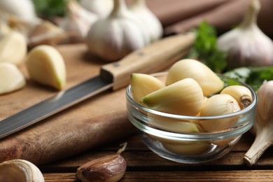 Photo of Fresh peeled garlic cloves in bowl on wooden table, closeup. Organic product