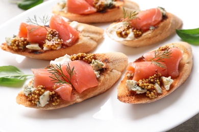 Photo of Tasty bruschettas with salmon and blue cheese on plate, closeup