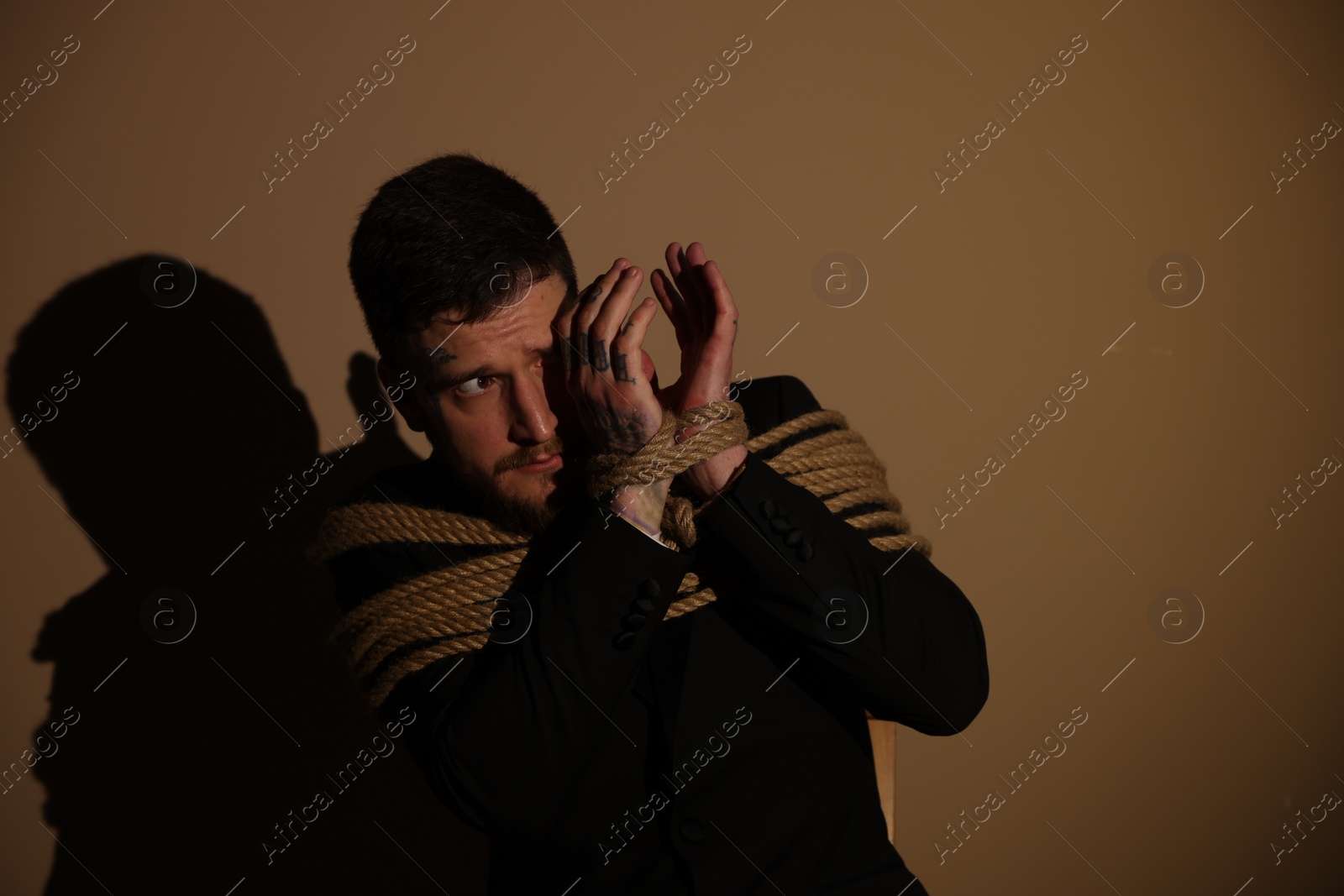 Photo of Scared man tied up and taken hostage on dark background. Space for text