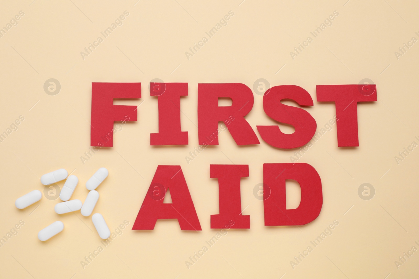 Photo of Words First Aid made of red letters and pills on beige background, flat lay