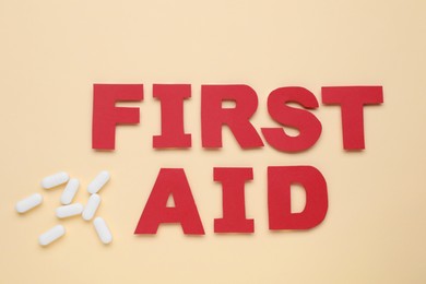 Words First Aid made of red letters and pills on beige background, flat lay