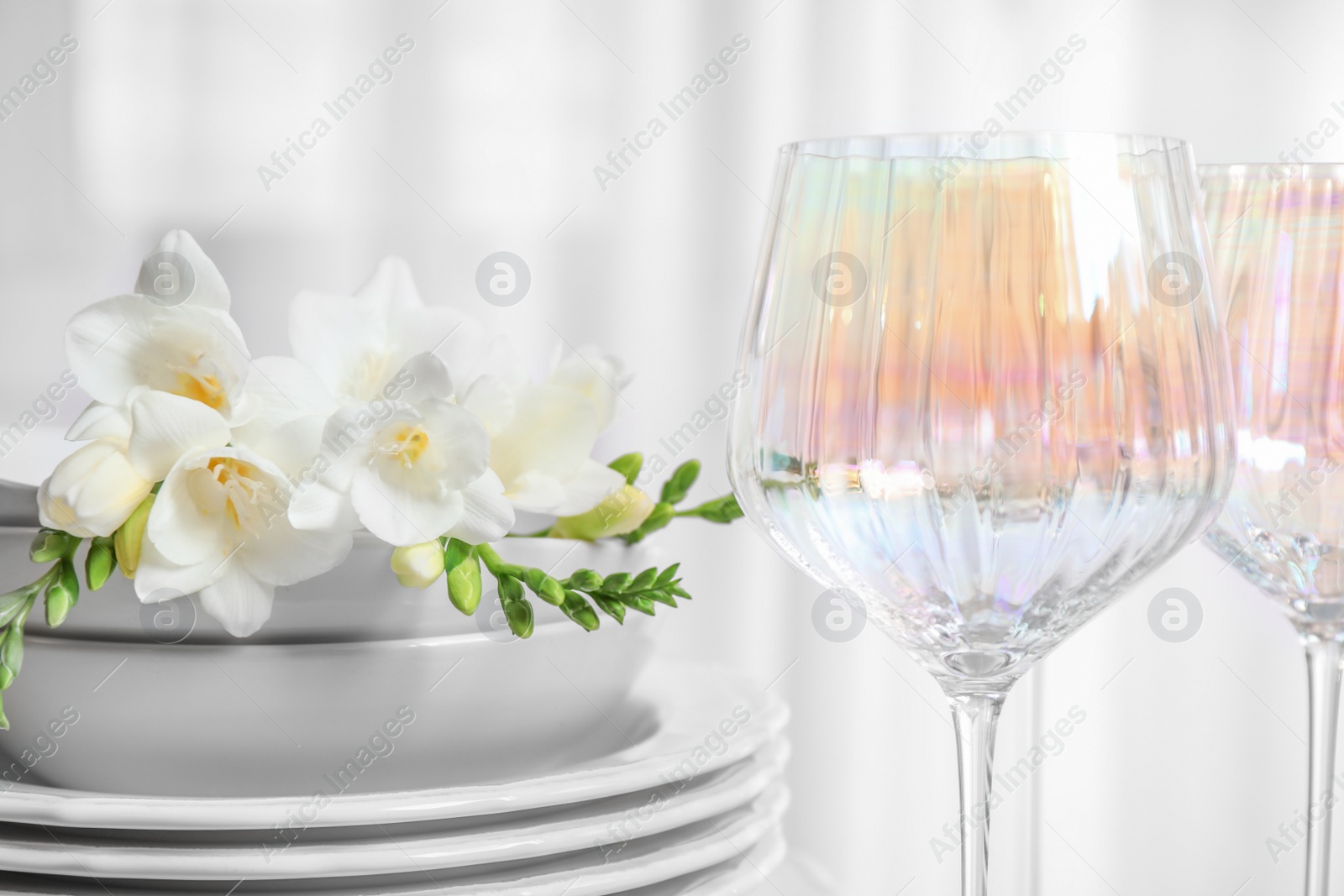 Photo of Set of glasses and dishes with flowers on light background, closeup