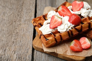 Photo of Board with delicious Belgian waffles, strawberry, whipped cream and chocolate sauce on wooden table, closeup. space for text
