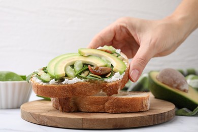 Woman taking tasty vegan sandwich with avocado, tomato and spinach at white marble table, closeup