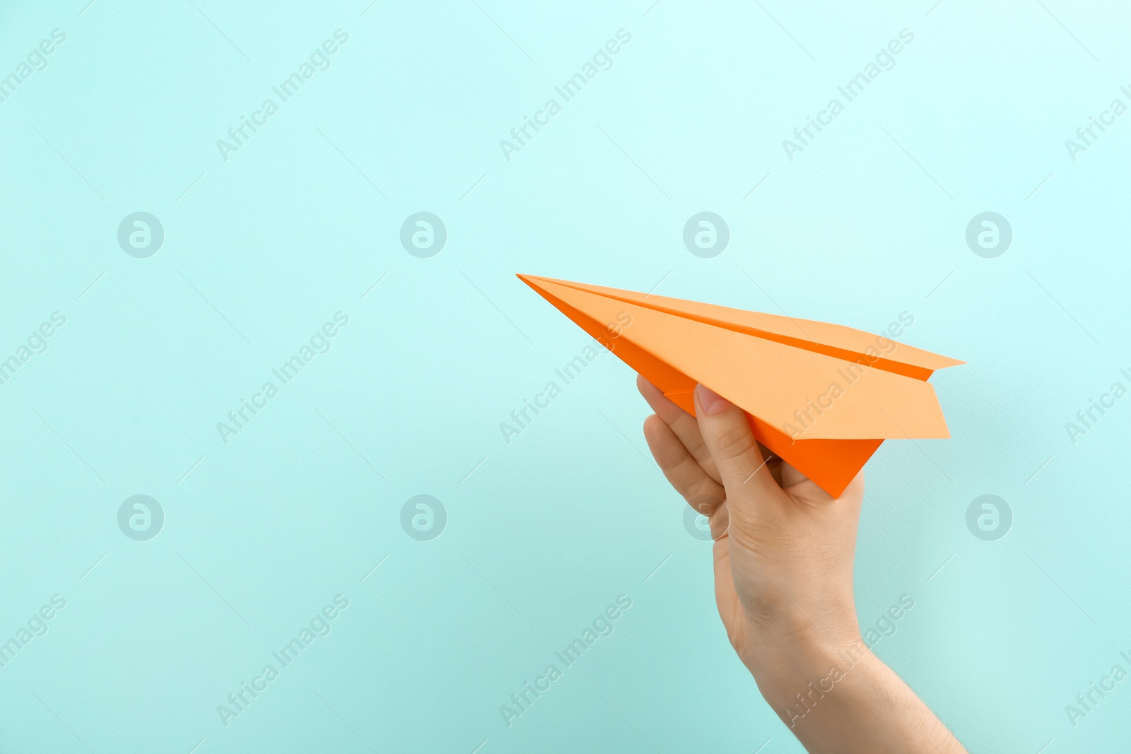 Photo of Woman holding paper plane on light blue background, closeup. Space for text