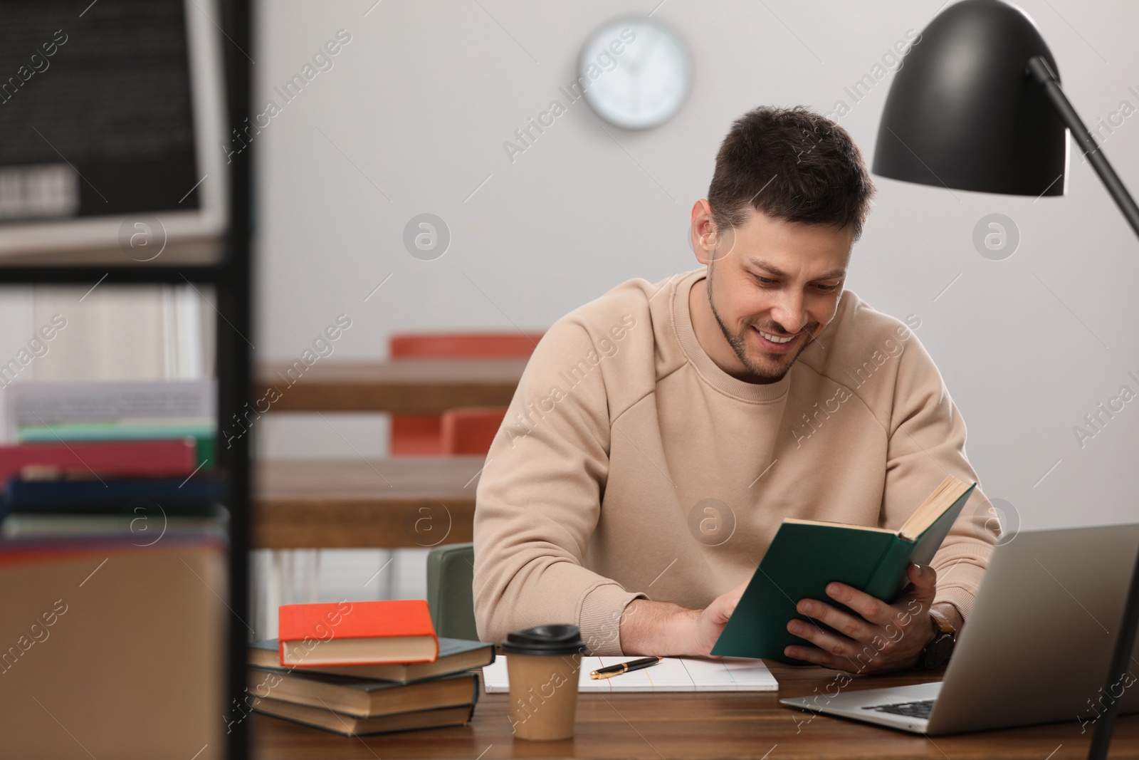 Photo of Man reading book at table in library