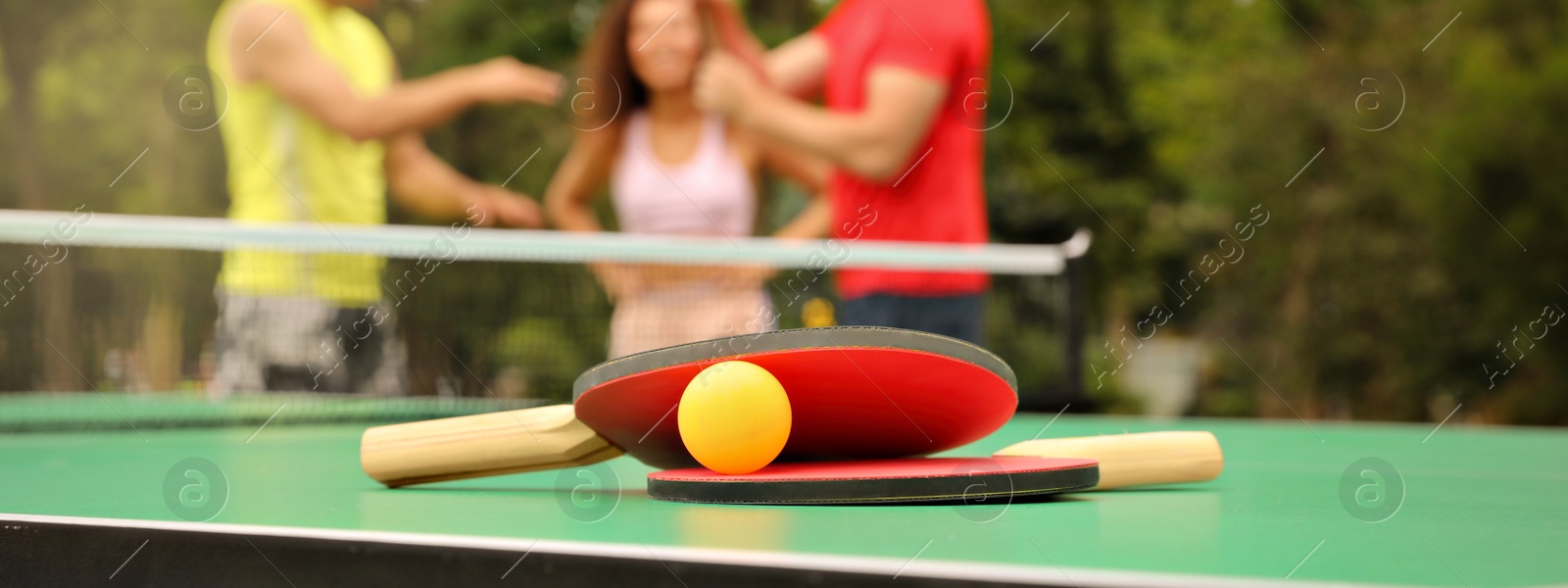 Image of Friends talking near ping pong table outdoors, focus on rackets and ball. Banner design