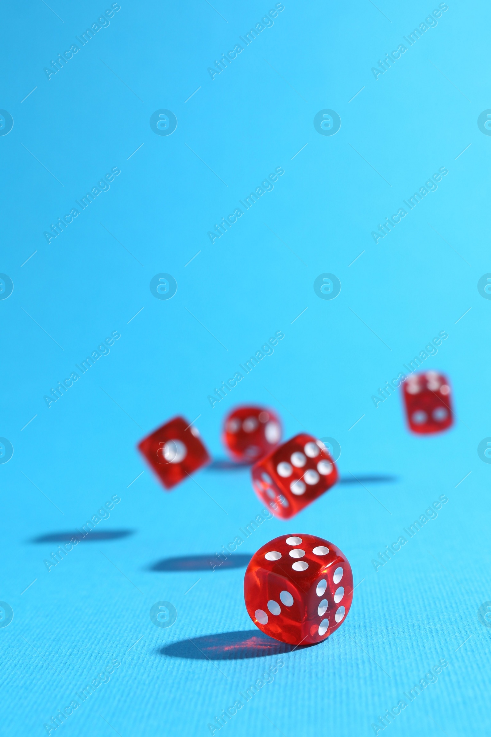 Photo of Many red game dices falling on light blue background. Space for text