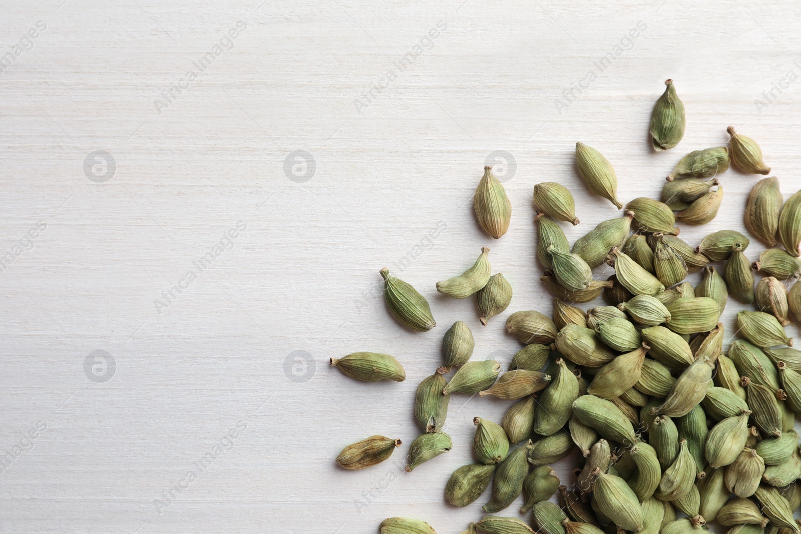 Photo of Pile of dry cardamom pods on white wooden table, top view. Space for text