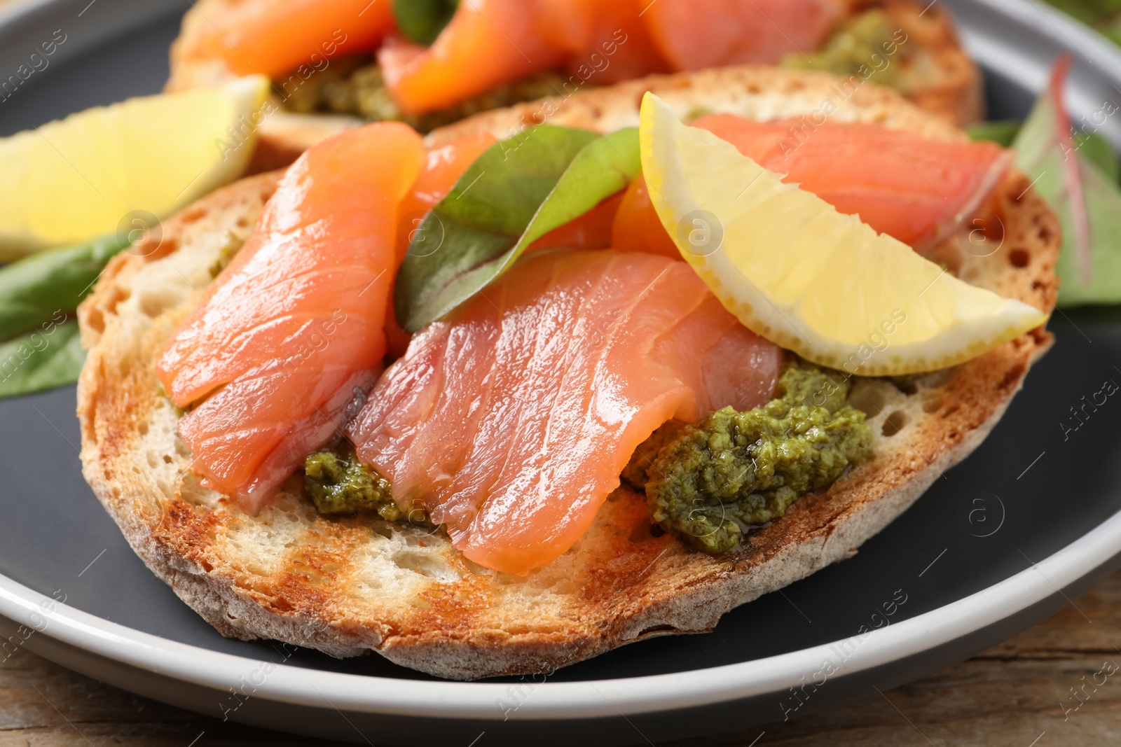 Photo of Delicious bruschetta with salmon and pesto sauce on wooden table, closeup