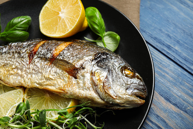 Photo of Delicious roasted fish with lemon on blue wooden table, closeup